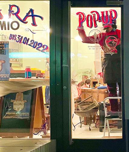 Ein junger Mann bringt ein Schild mit der Aufschrift "Pop-Up-Store" in einem leerstehenden Laden an.